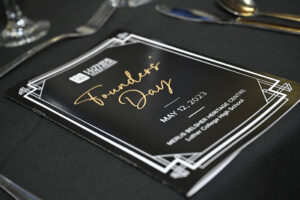 Event program for Founders Day at Luther College High School, held on May 12, 2023, at Merlis Belsher Heritage Centre, displayed on a black tablecloth with cutlery in the background.