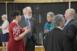 Group of professionals networking at a formal event; people dressed in business attire holding drinks, engaging in conversation against a black curtain backdrop—corporate gathering, business networking, formal event interaction.