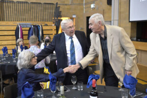 Elderly people shaking hands at a formal event in a banquet hall with elegantly set tables.