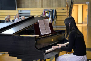 Young Woman Playing Piano During Recital in a Concert Hall, Sheet Music Displayed on Grand Piano.