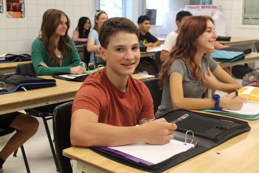 Students in a classroom, teenagers smiling and participating in learning activities, educational environment, diverse group of high school students, happy and engaging study sessions.